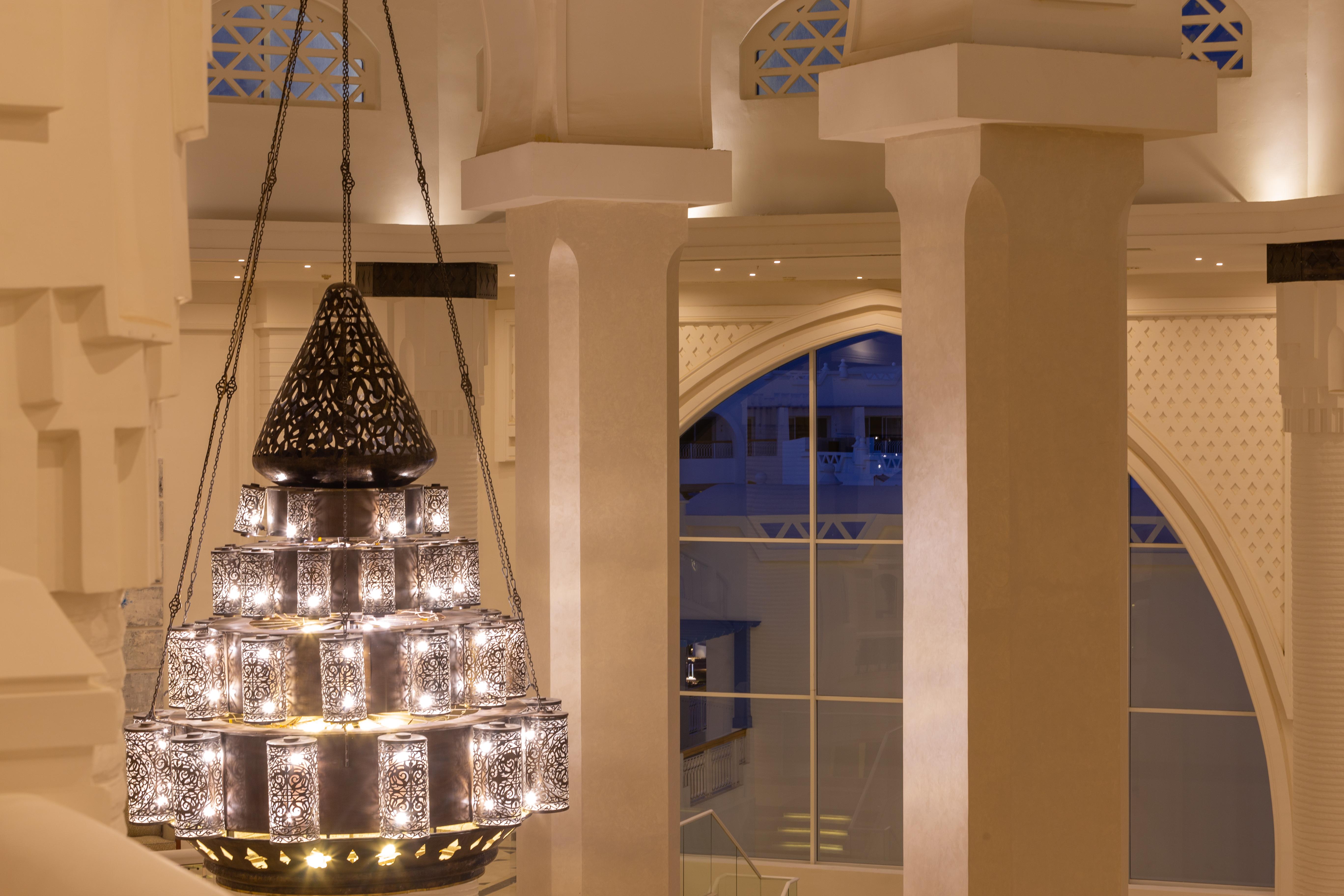 Pickalbatros Palace Sharm - "Aqua Park" Esterno foto The photo shows a beautifully designed chandelier hanging from the ceiling of a spacious interior. The chandelier features a structure with multiple levels and includes ornate patterns, likely made of metal or glass, that diffuse light elegantly. The