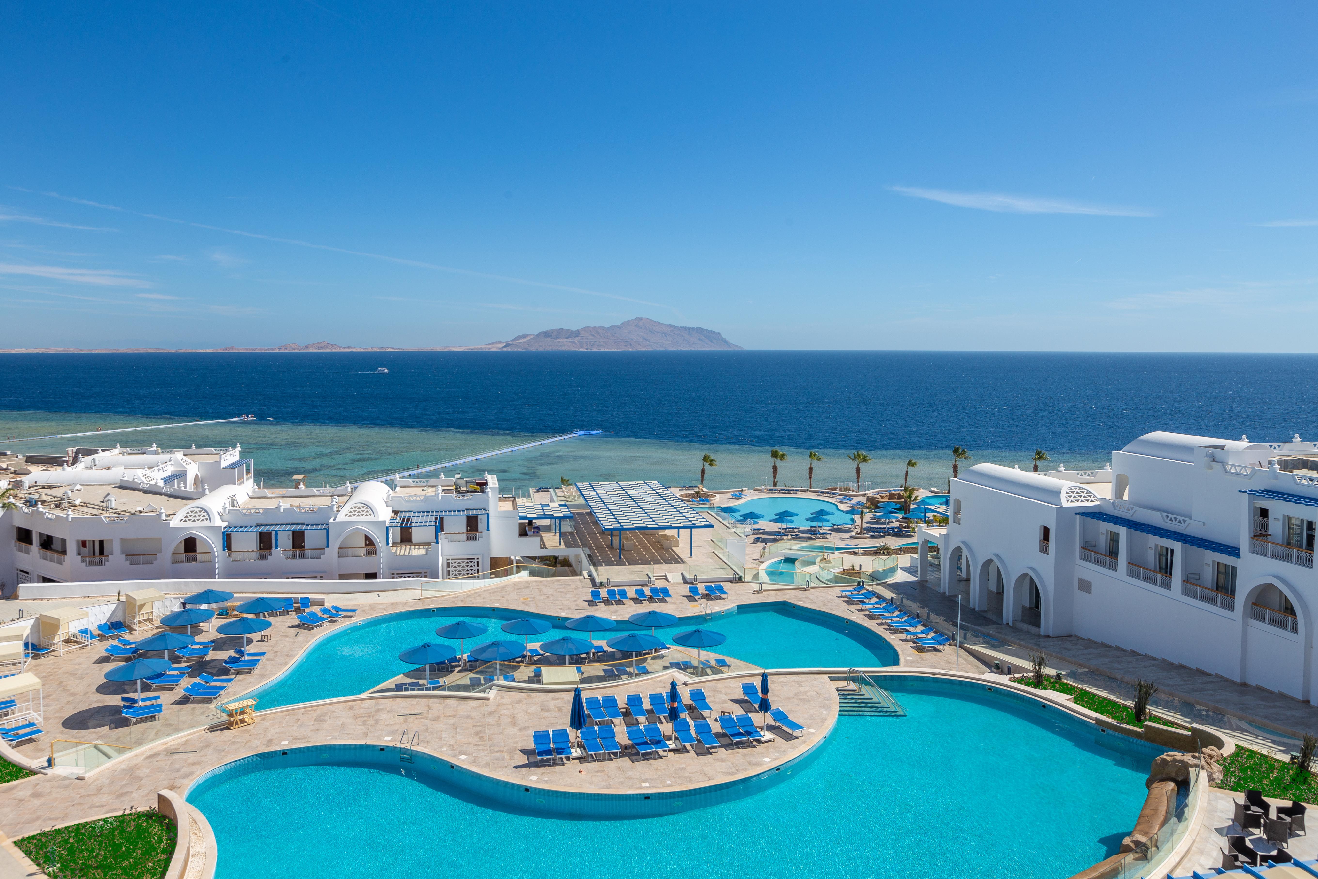 Pickalbatros Palace Sharm - "Aqua Park" Esterno foto The image shows a beautiful seaside resort with multiple swimming pools surrounded by lounge chairs. The pools are designed in various shapes, and the area is adorned with sun umbrellas. In the background, you can see the clear blue ocean and a dista
