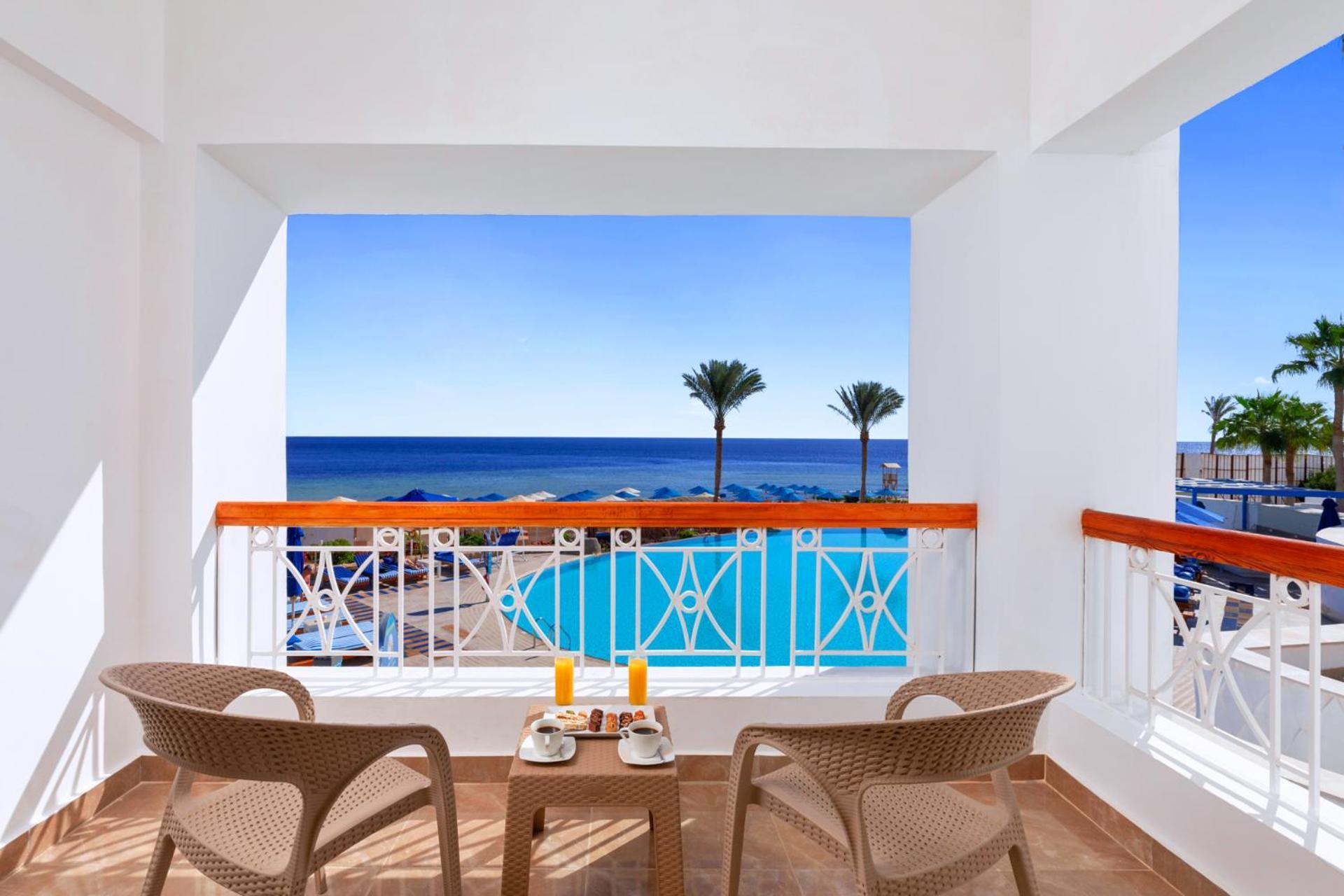 Pickalbatros Palace Sharm - "Aqua Park" Esterno foto The photo shows a bright and inviting balcony with two wicker chairs and a small table. On the table, there are two glasses of orange juice and a plate of food. The balcony overlooks a beautiful view of the ocean, with the deep blue water stretching 
