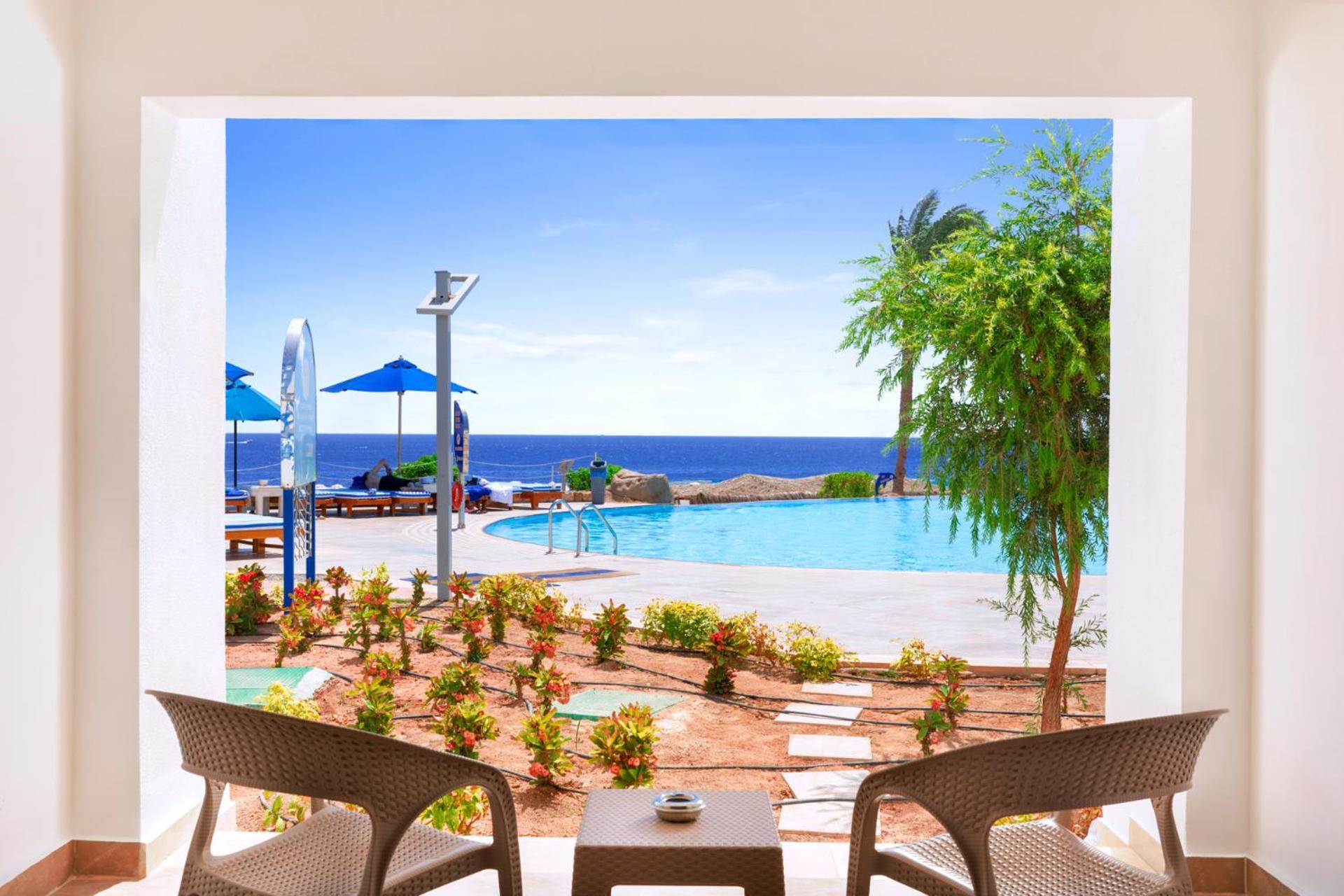 Pickalbatros Palace Sharm - "Aqua Park" Esterno foto The photo shows a serene view from inside a space looking out onto a beautiful scene. In the foreground, there are two comfortable chairs positioned around a small table, suggesting a cozy place to relax. Beyond the seating area, there is a landscape