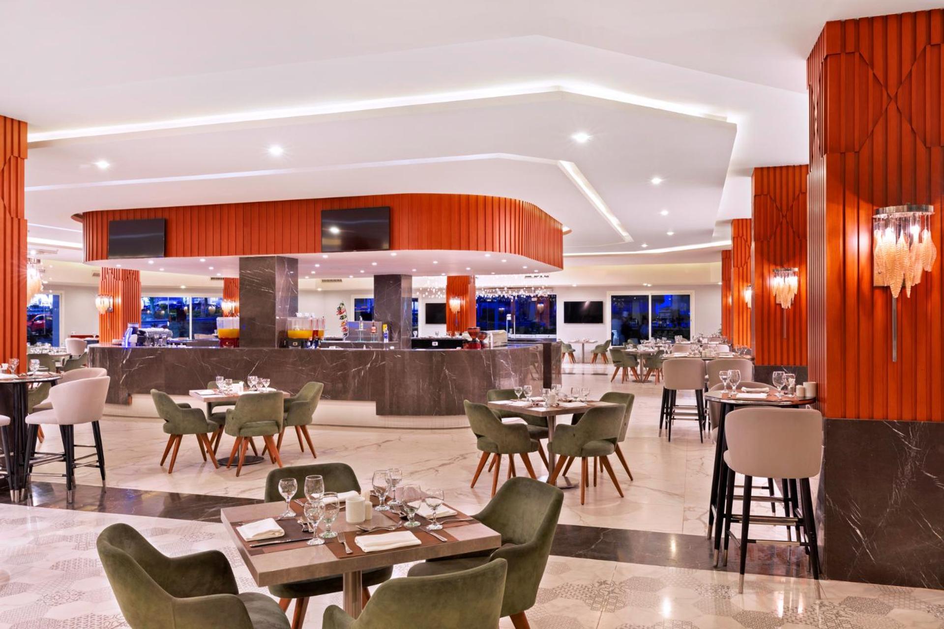 Pickalbatros Palace Sharm - "Aqua Park" Esterno foto The photo depicts a modern restaurant interior. The space features a stylish bar area with a curved counter and bright lighting. There are multiple dining tables set with tableware, including plates and glasses. The design includes a mix of seating o