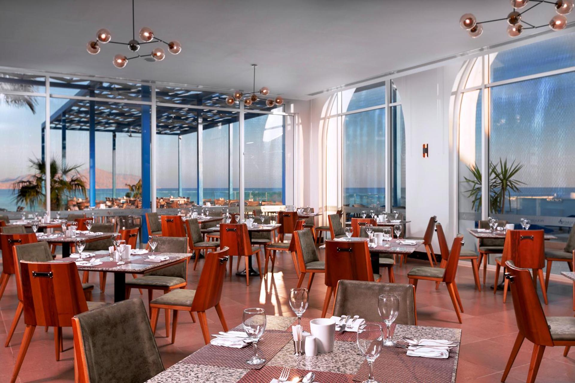Pickalbatros Palace Sharm - "Aqua Park" Esterno foto The photo shows a modern restaurant interior featuring multiple dining tables arranged neatly across the space. The tables are set with utensils, glasses, and decorations, indicating readiness for guests. Large windows allow plenty of natural light t